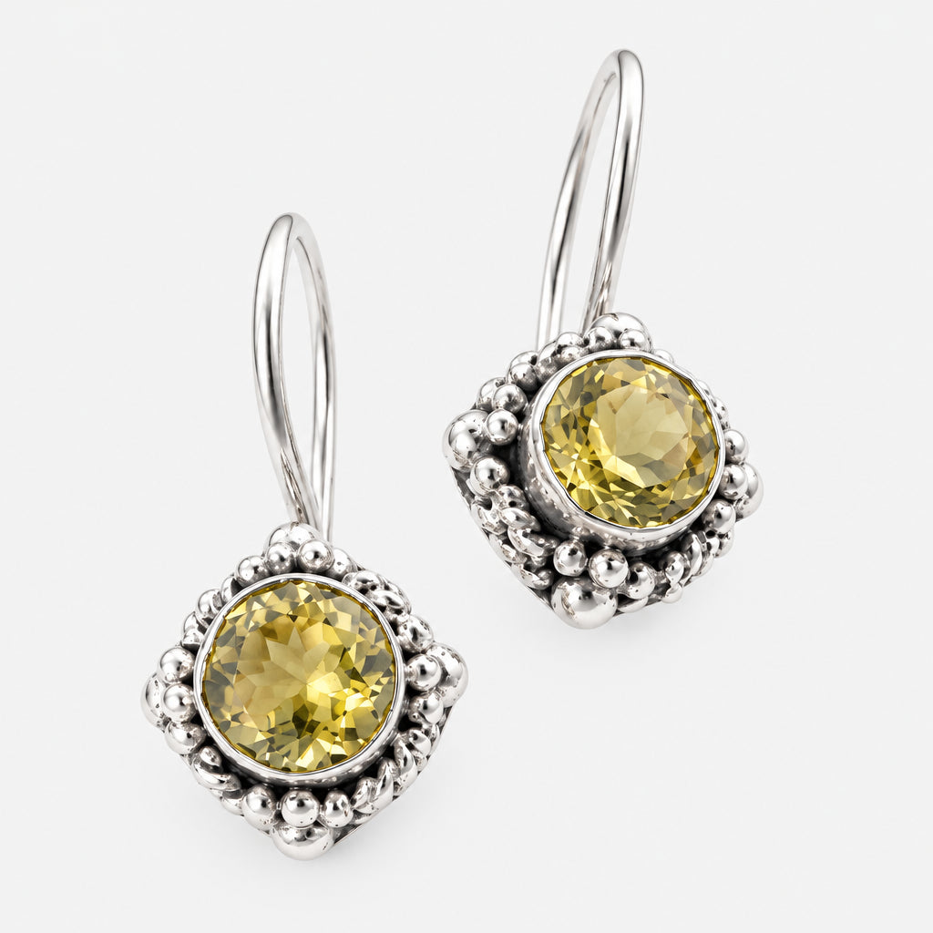 A pair of silver drop earrings featuring round, faceted olive-green gemstones surrounded by textured silver bezels and small bead details, set against a plain white background.
