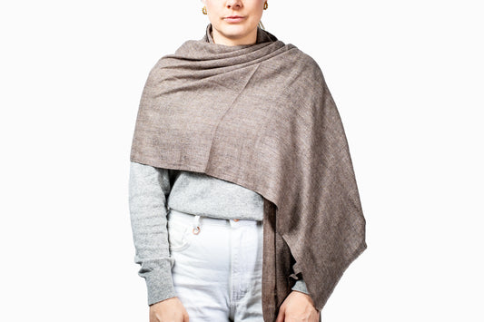 Person wearing a brown shawl over a gray sweater and light blue jeans on a white background