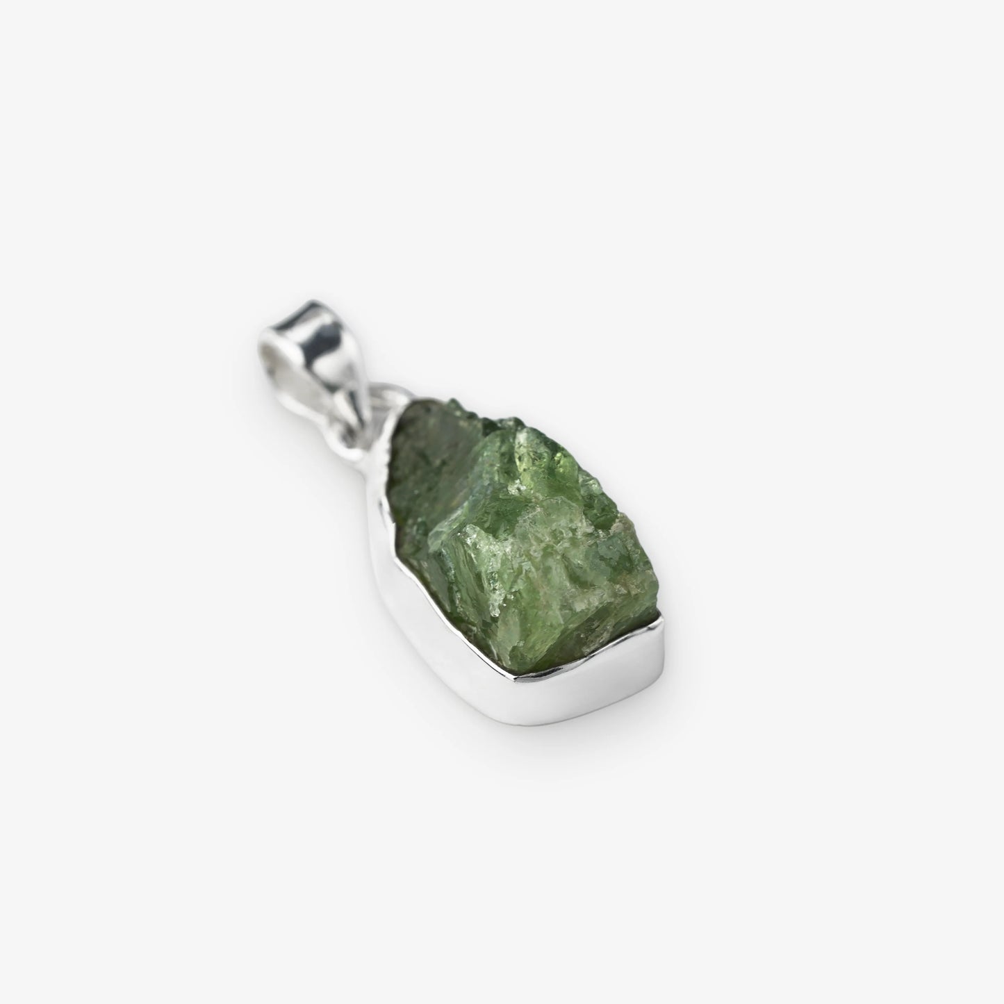 A raw green gemstone peridot pendant set in a polished silver bezel with a silver bail, shown on a light gray background.