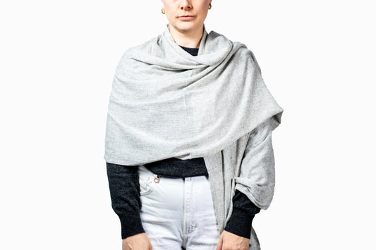Person wearing a silver grey pashmina shawl over a black top and white pants on a white background GRIHA