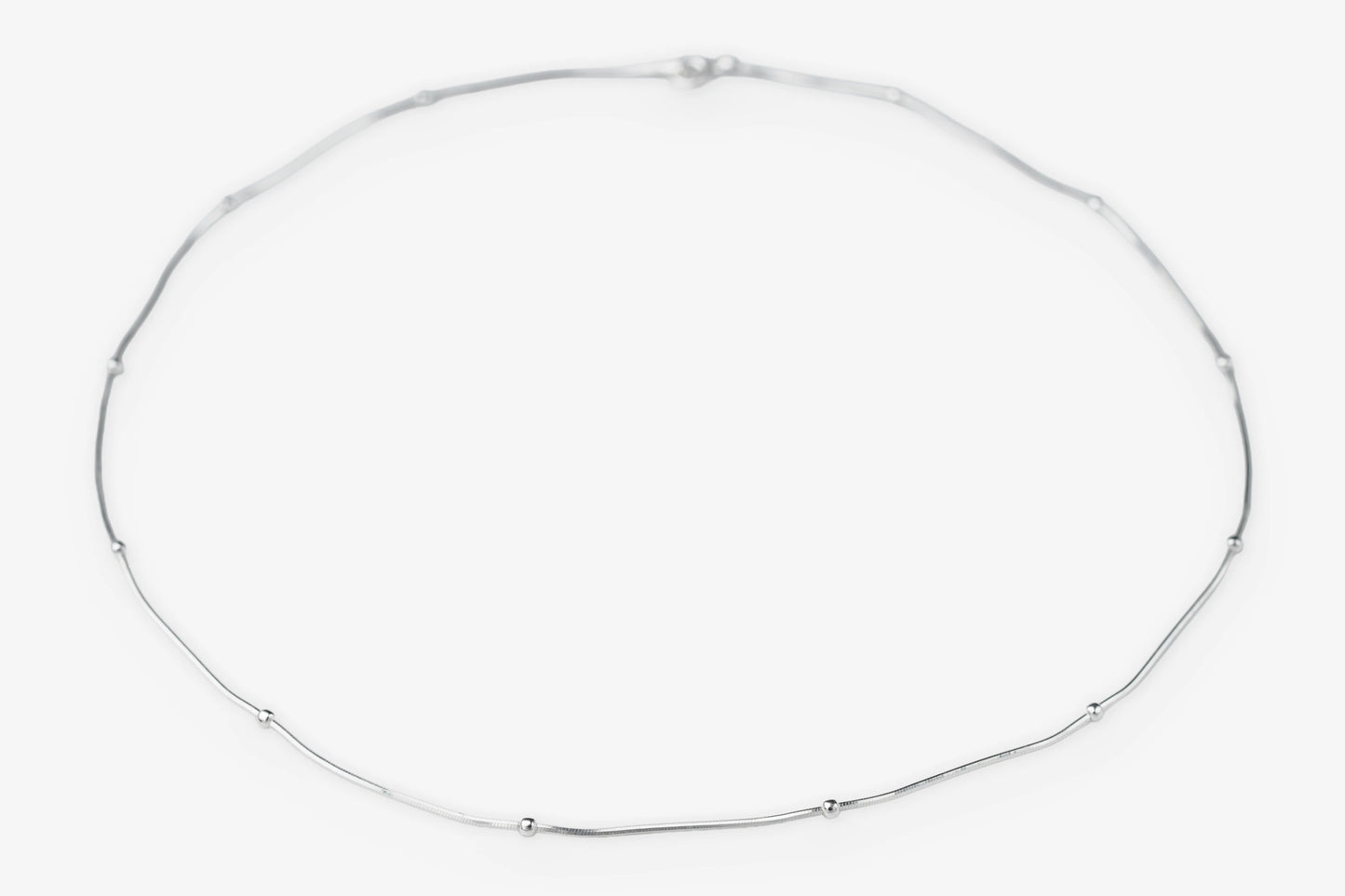 A delicate silver chain necklace arranged in a loose circle on a plain white background.