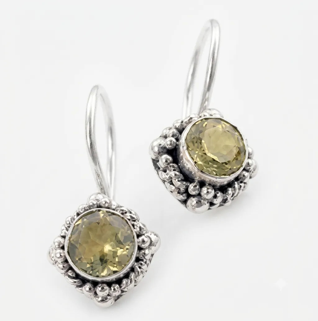 A pair of silver drop earrings featuring round, faceted olive-green gemstones surrounded by textured silver bezels and small bead details, set against a plain white background.