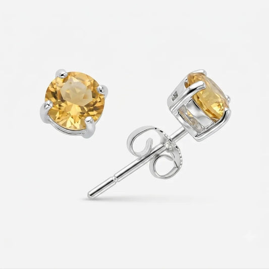 A pair of round-cut yellow gemstone stud earrings in silver prong settings, with one earring facing forward and the other angled to show the post and butterfly back, on a light gray background.