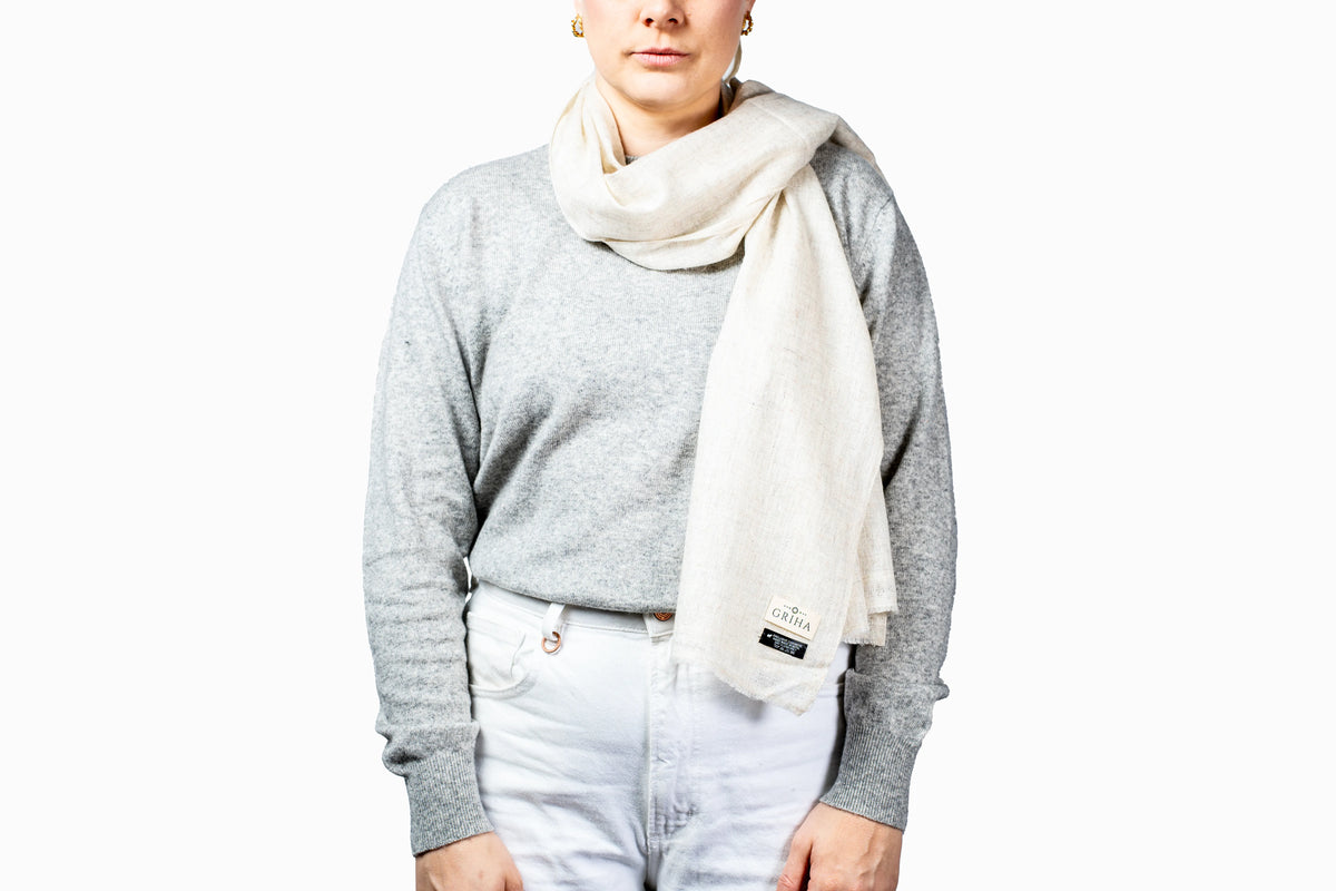 Person wearing a gray sweater and white scarf with a visible brand logo on a white background