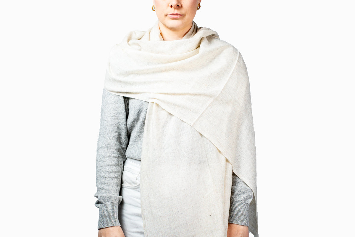 Person wearing a white pashmina scarf on a plain background
