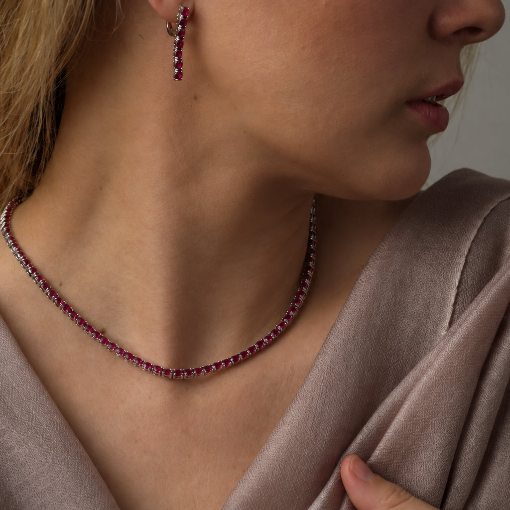 Model wearing ruby tennis necklace set in 925 sterling silver and also wearing ruby hook drop earrings. Model has elegant soft light brown pashmina draped over the shoulder.