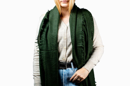 Person wearing a cashmere green scarf, light-colored shirt, and blue jeans on a white background