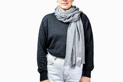 Person wearing a grey pashmina scarf with a visible brand logo on a white background