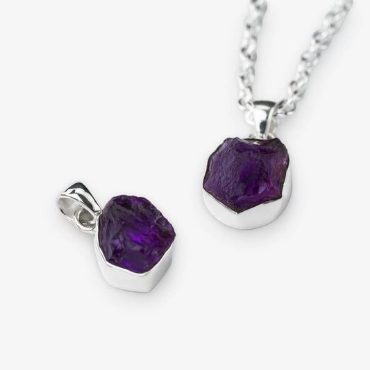 A silver necklace and pendant set featuring a raw, faceted purple amethyst gemstone in a polished silver bezel setting, shown on a clean white background.