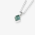A silver chain necklace with a small, polished silver pendant holding a rough, faceted aquamarine green gemstone, shown on a light gray background.