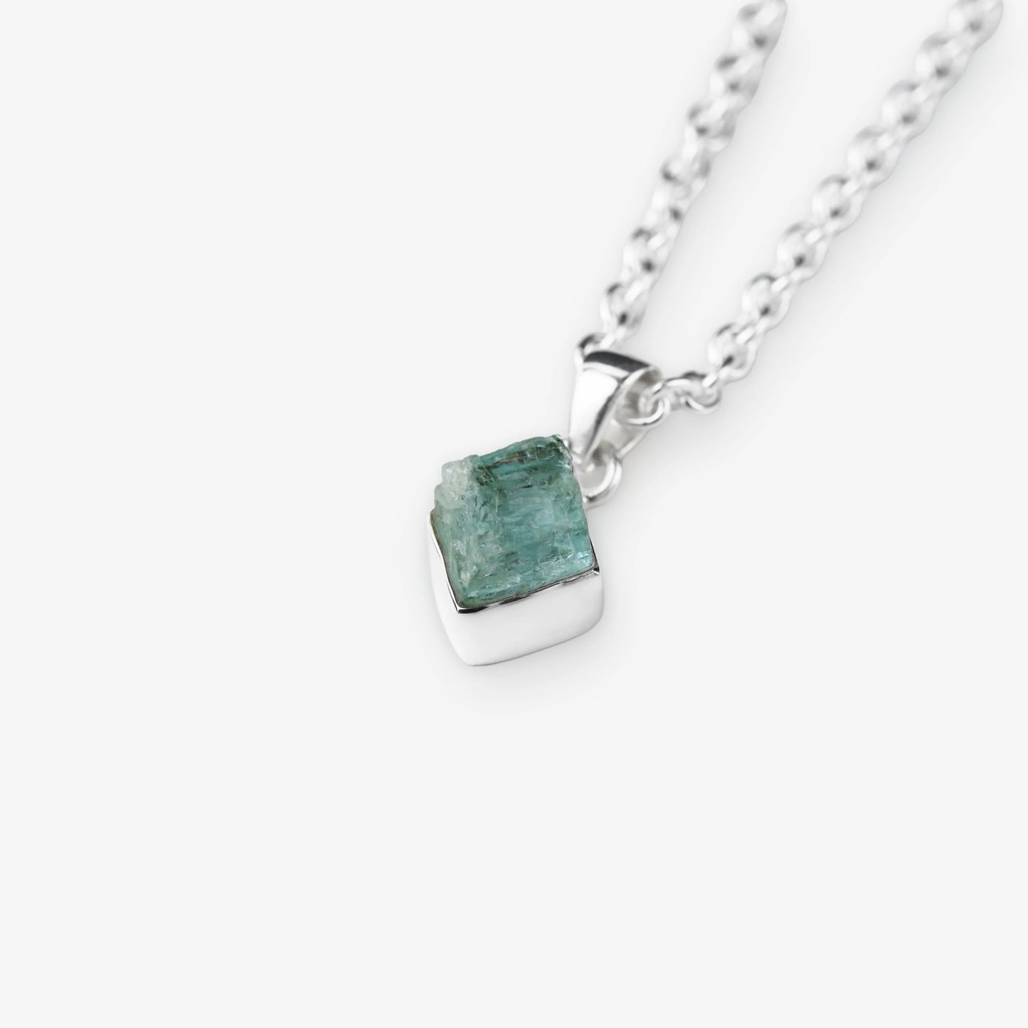 A silver chain necklace with a small, polished silver pendant holding a rough, faceted aquamarine green gemstone, shown on a light gray background.