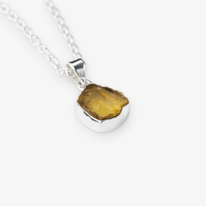 A silver chain necklace with a polished sterling silver pendant holding a raw, irregular-cut yellow citrine gemstone, shown on a light gray background.