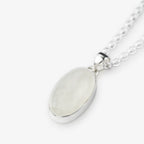 An oval pendant necklace featuring a milky white, iridescent moonstone set in a polished silver bezel, suspended from a silver chain against a light gray background.