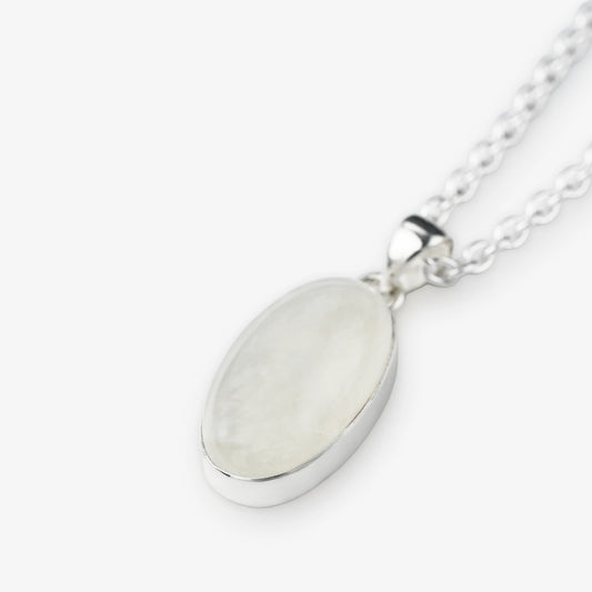 An oval pendant necklace featuring a milky white, iridescent moonstone set in a polished silver bezel, suspended from a silver chain against a light gray background.