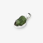 A raw green peridot gemstone pendant set in a polished silver bezel, shown on a light gray background.