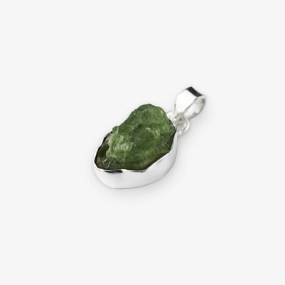 A raw green peridot gemstone pendant set in a polished silver bezel, shown on a light gray background.
