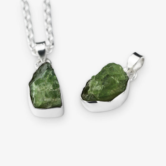 Two raw green peridot gemstone pendants in silver bezel settings, one hanging from a silver chain and one displayed flat, on a light gray background.