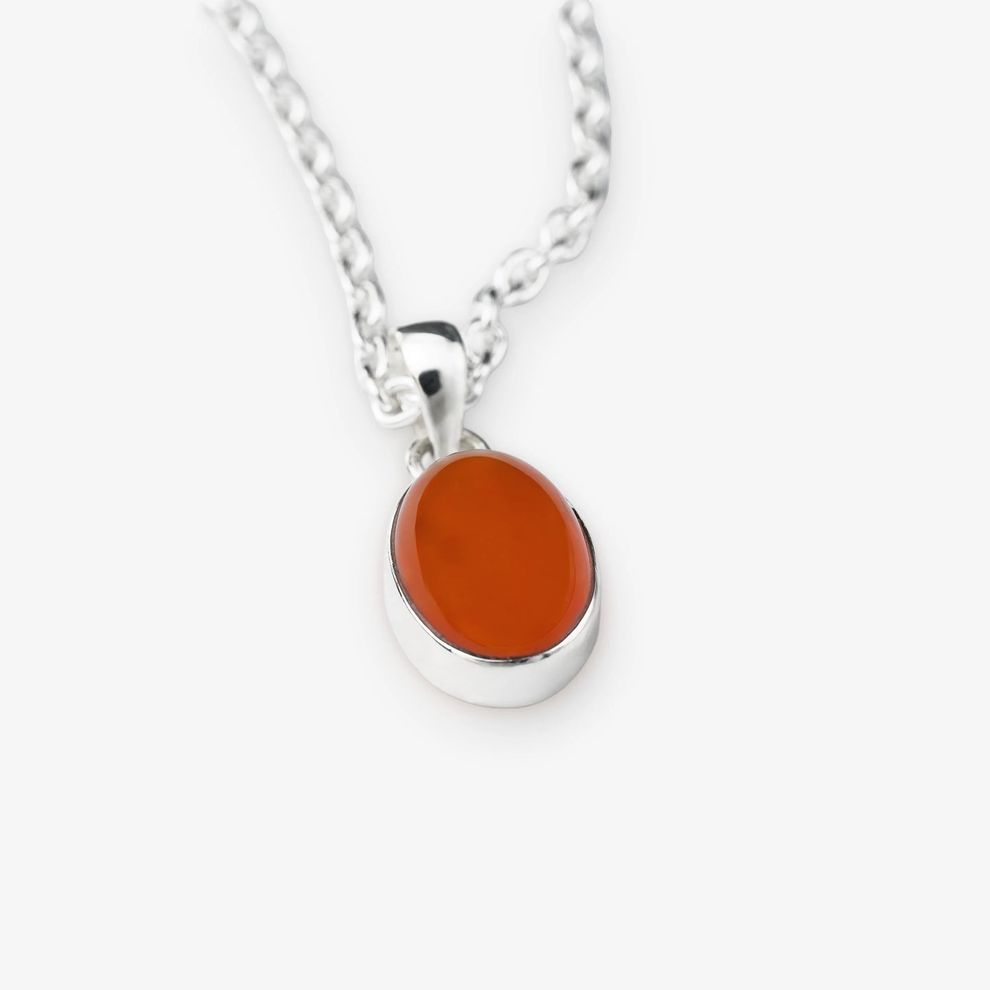 A silver chain necklace with an oval pendant featuring a smooth, polished orange carnelian stone in a silver bezel setting, shown against a light gray background.
