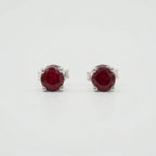 Pair of oval deep red gemstone stud earrings in silver-coloured four-prong settings on a white background.