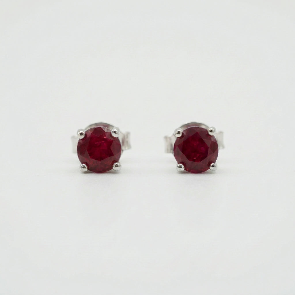 Pair of oval deep red gemstone stud earrings in silver-coloured four-prong settings on a white background.