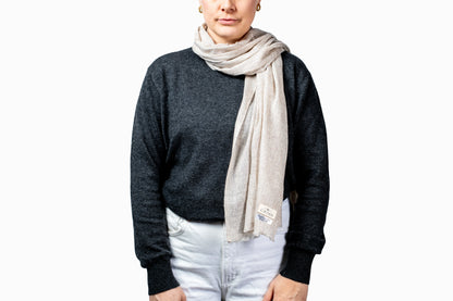 Person wearing a dark sweater and light natural beige pashmina scarf on a white background GRIHA