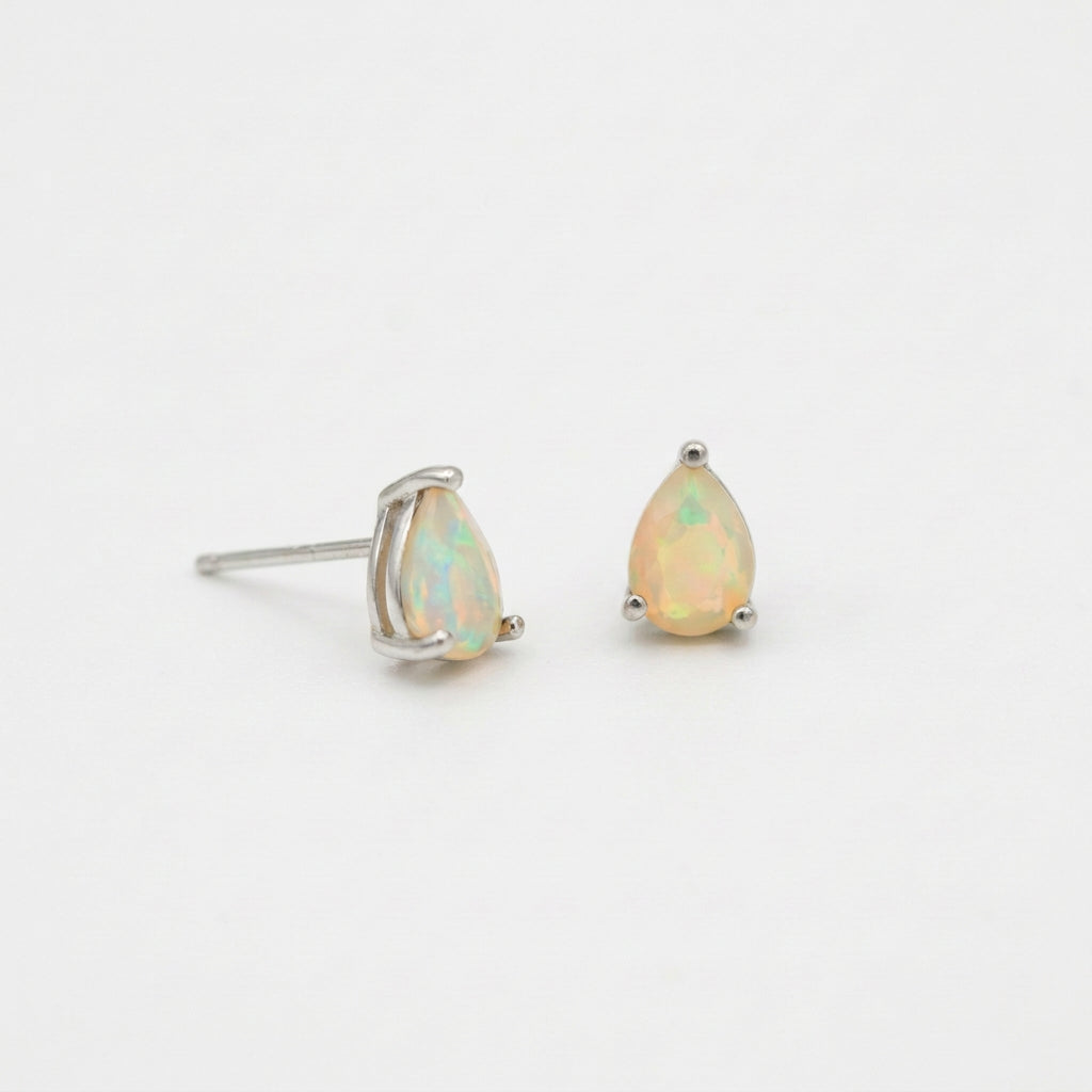 A pair of silver stud earrings featuring teardrop-shaped opal gemstones with a soft iridescent yellow and green play-of-color, set against a plain white background.