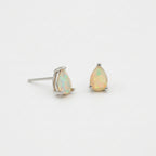 A pair of silver stud earrings featuring teardrop-shaped opal gemstones with a soft iridescent yellow and green play-of-color, set against a plain white background.