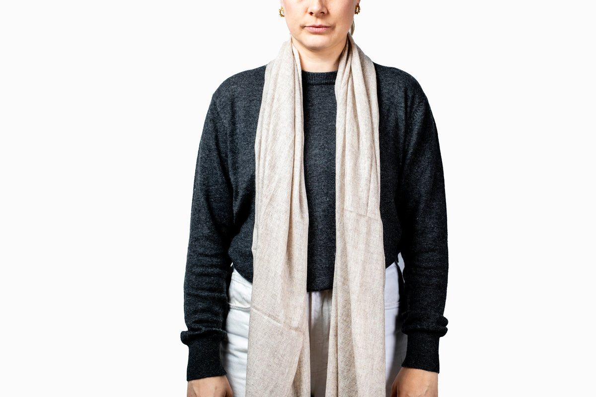 Person wearing a beige pashmina scarf with a plain background