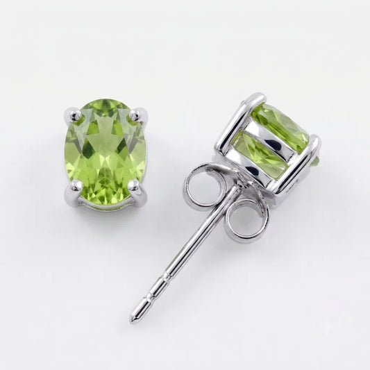 A pair of oval peridot stud earrings in silver settings, one showing the front view with the faceted green gemstone and the other showing the side profile with the post and butterfly back, on a white background.