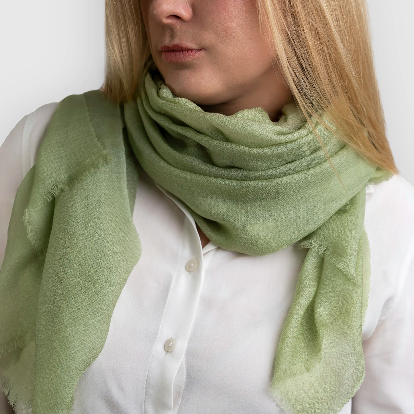 Sage green pashmina shawl scarf wrapped around model neck wearing a white blouse on grey background