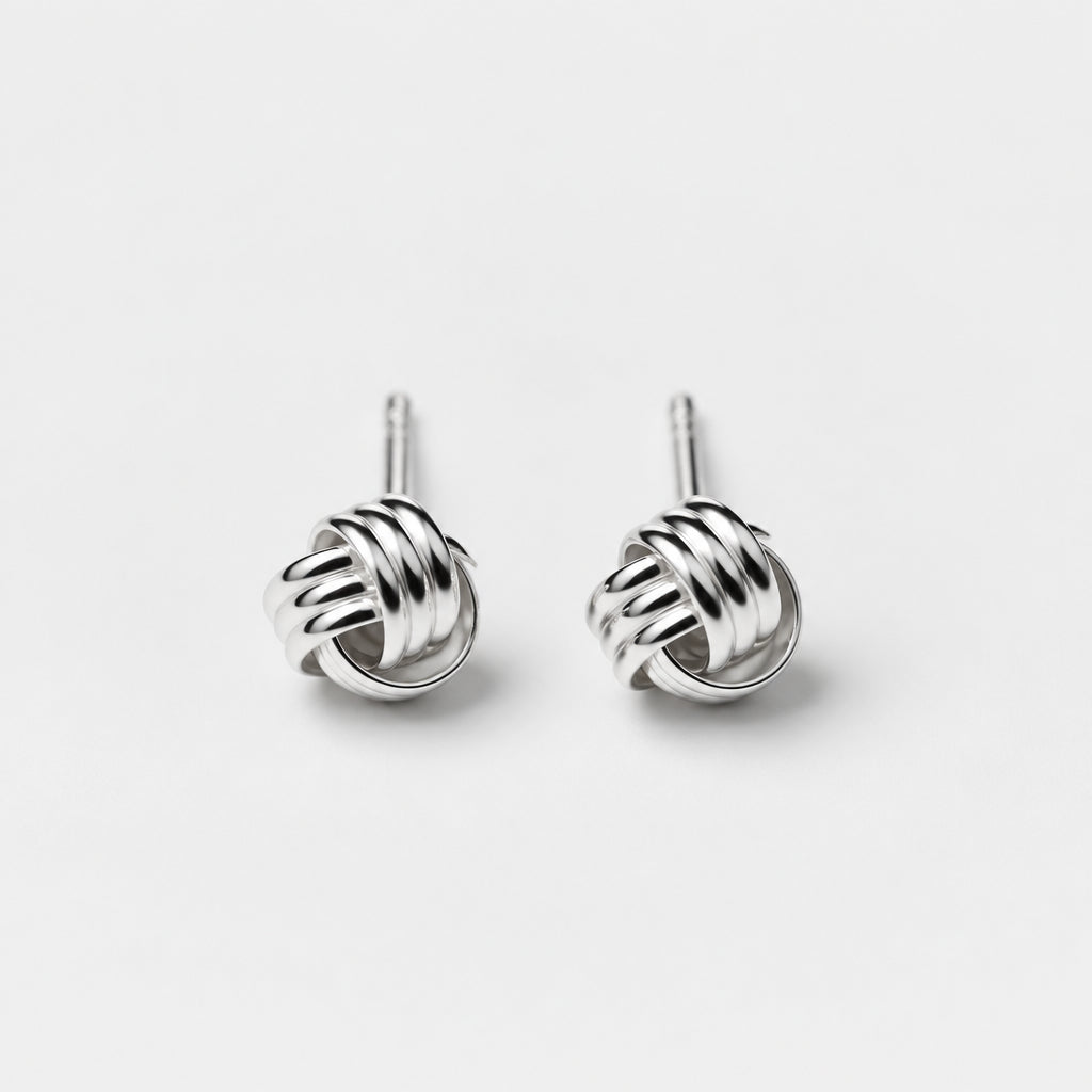A pair of sterling silver stud earrings with an intricate knot design on a beige background.