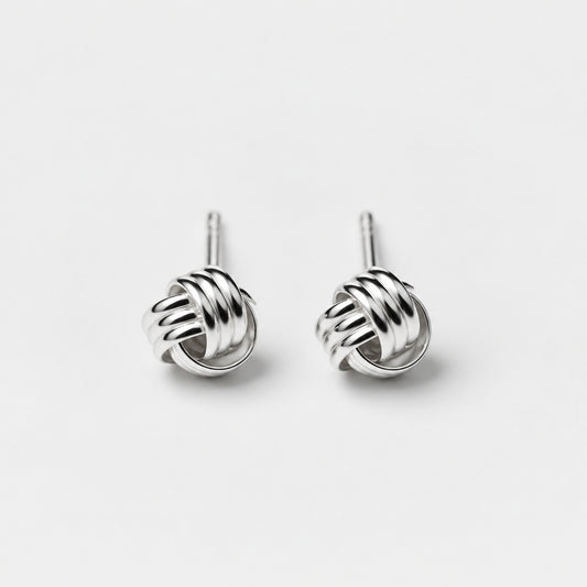 A pair of sterling silver stud earrings with an intricate knot design on a beige background.