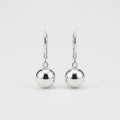 A pair of polished silver leverback earrings with smooth, spherical drop charms, shown against a clean, light gray background.