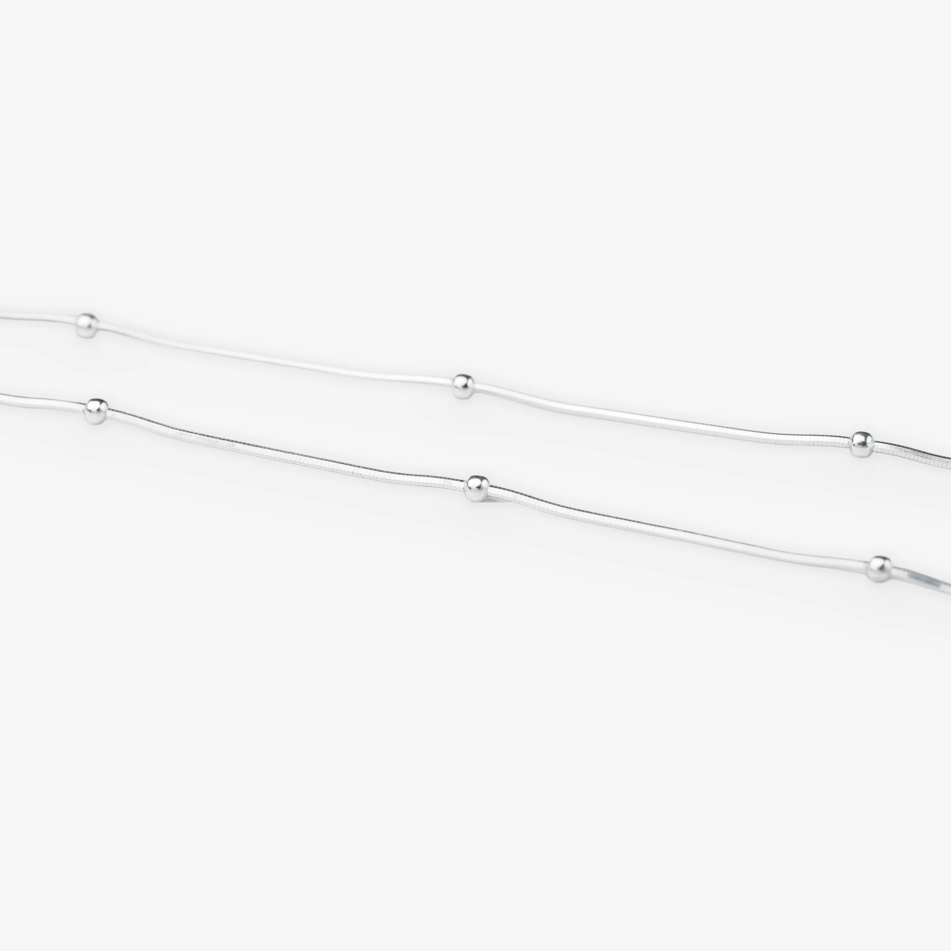 A delicate silver chain necklace featuring evenly spaced, small polished round beads, shown against a clean white background.