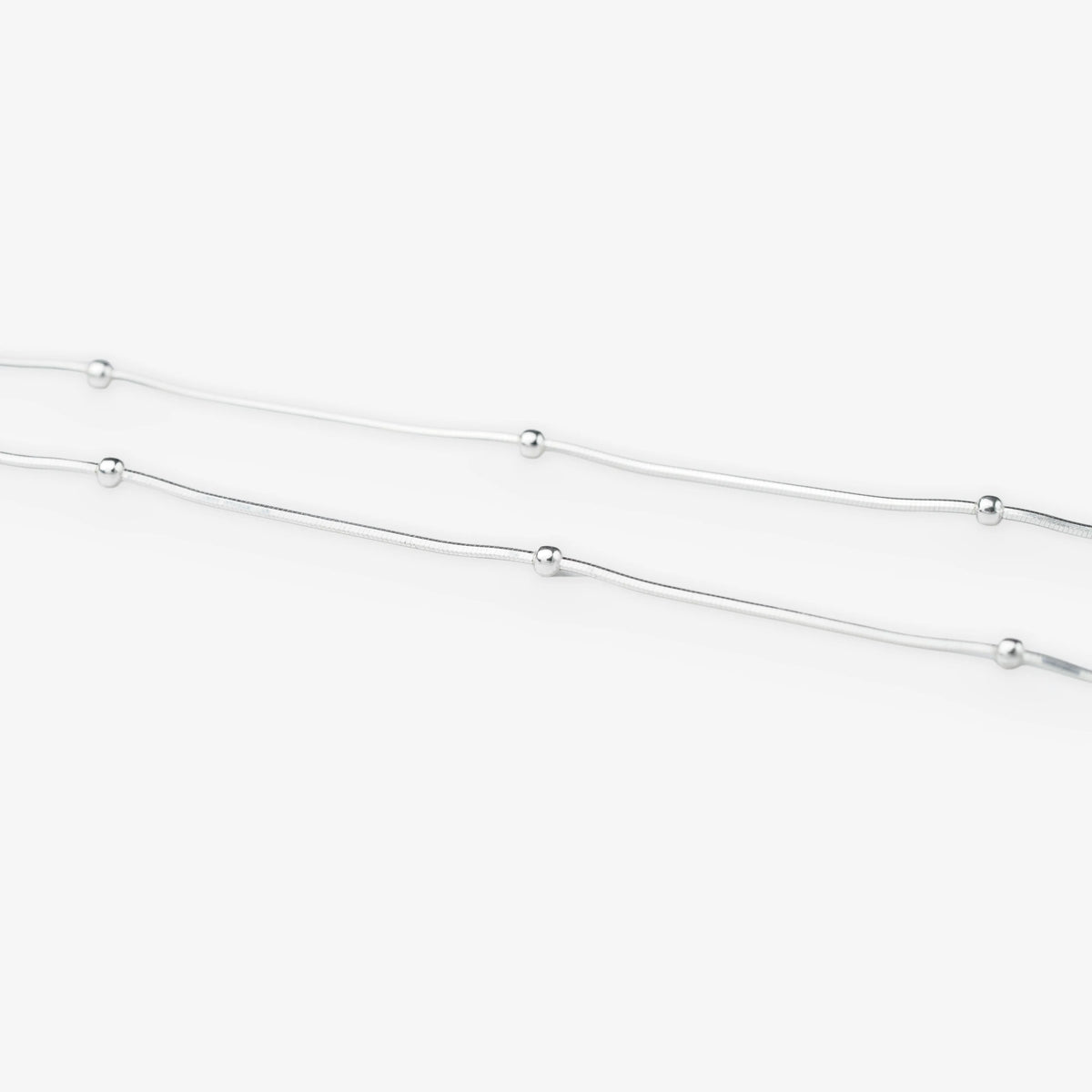 A delicate silver chain necklace featuring evenly spaced, small polished round beads, shown against a clean white background.