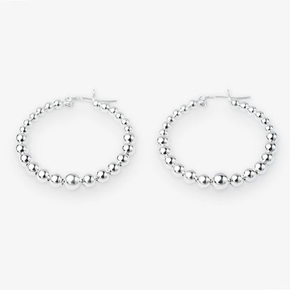 A pair of silver hoop earrings with a beaded, textured design, displayed against a clean white background.