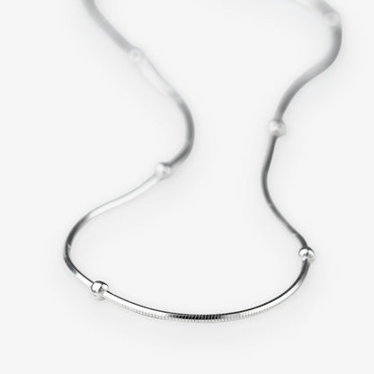 A silver snake chain necklace with small, evenly spaced spherical bead accents, displayed on a clean white background.