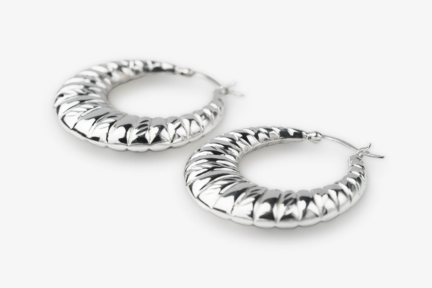 A pair of textured silver hoop earrings with a ribbed, snake-like pattern, displayed on a clean white background.