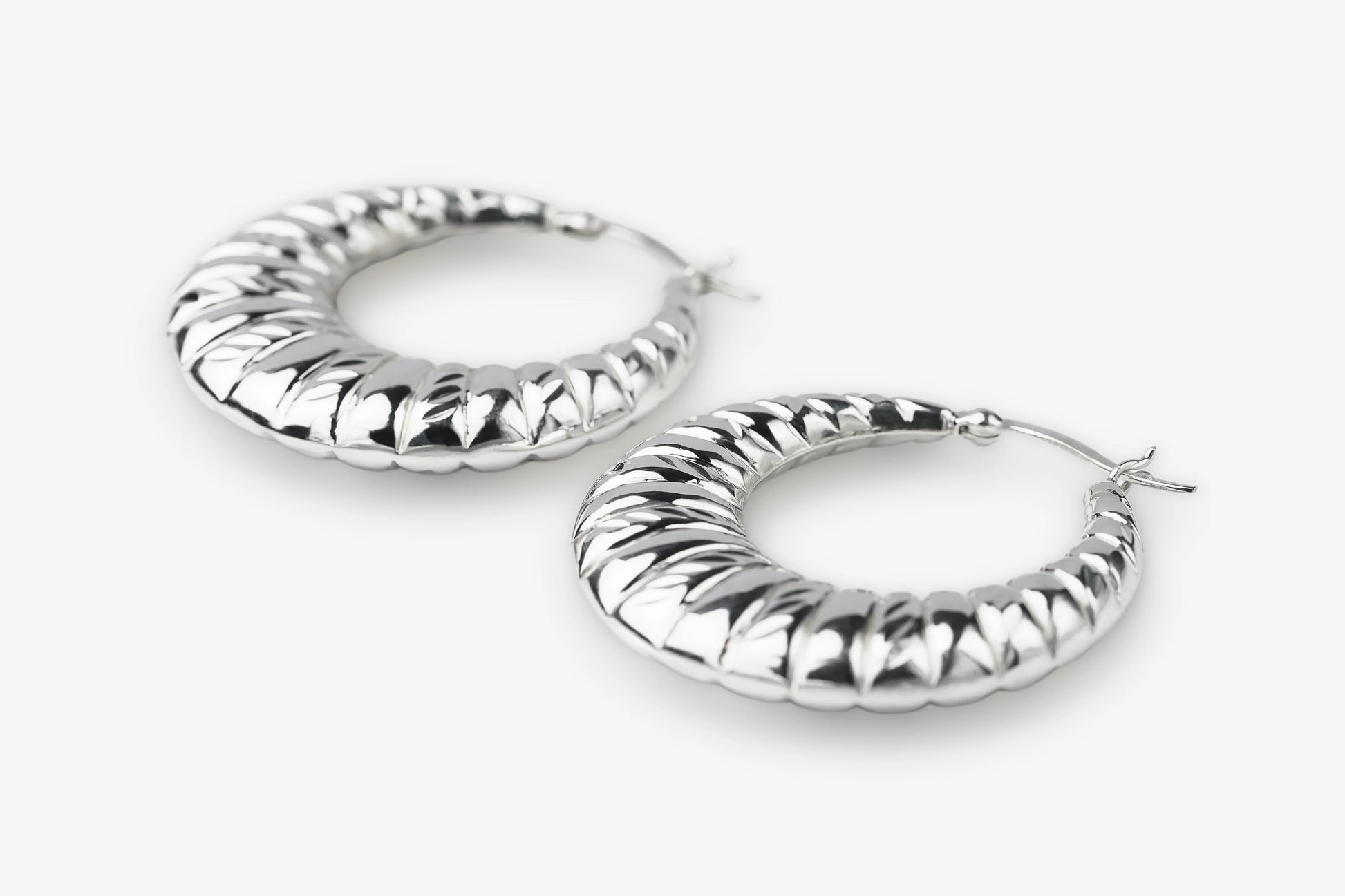 A pair of textured silver hoop earrings with a ribbed, snake-like pattern, displayed on a clean white background.