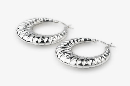 A pair of textured silver hoop earrings with a ribbed, snake-like pattern, displayed on a clean white background.