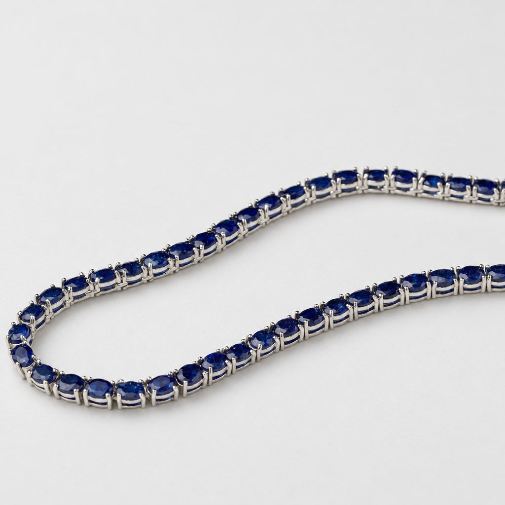 A tennis-style necklace with dark blue oval gemstones set in a silver-toned metal, photographed on a plain light background.