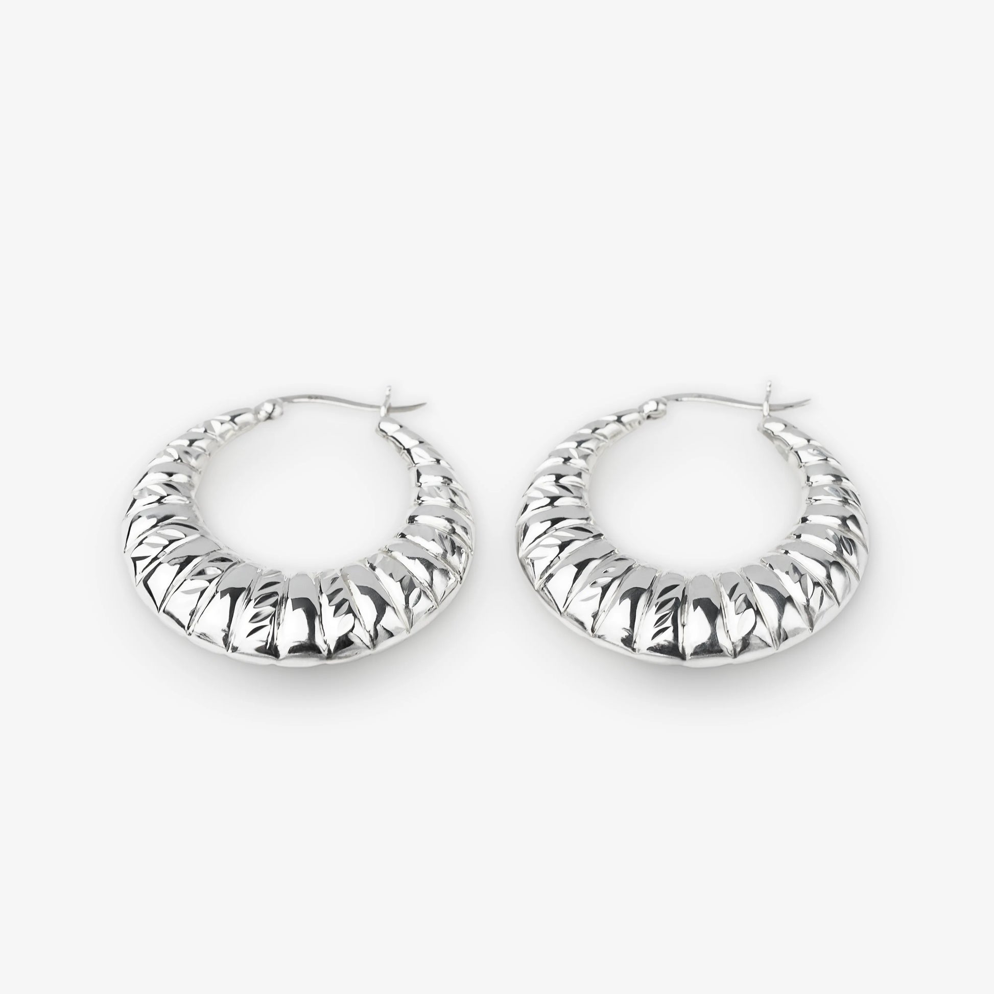 A pair of textured silver hoop earrings with a ribbed, ridged outer surface, displayed on a clean light gray background.