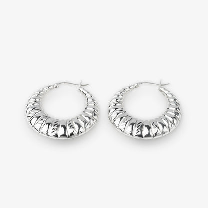 A pair of textured silver hoop earrings with a ribbed, ridged outer surface, displayed on a clean light gray background.