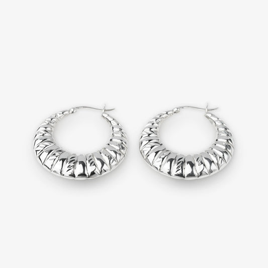A pair of textured silver hoop earrings with a ribbed, ridged outer surface, displayed on a clean light gray background.