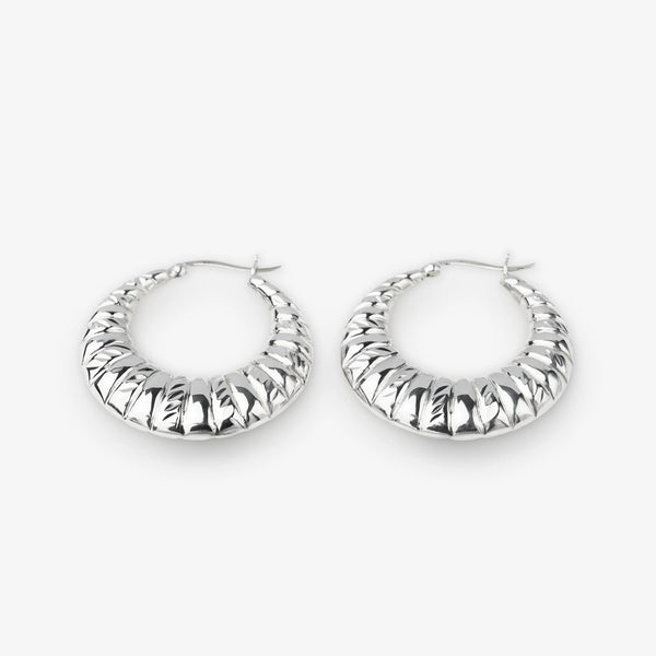 A pair of textured silver hoop earrings with a ribbed, ridged outer surface, displayed on a clean light gray background.