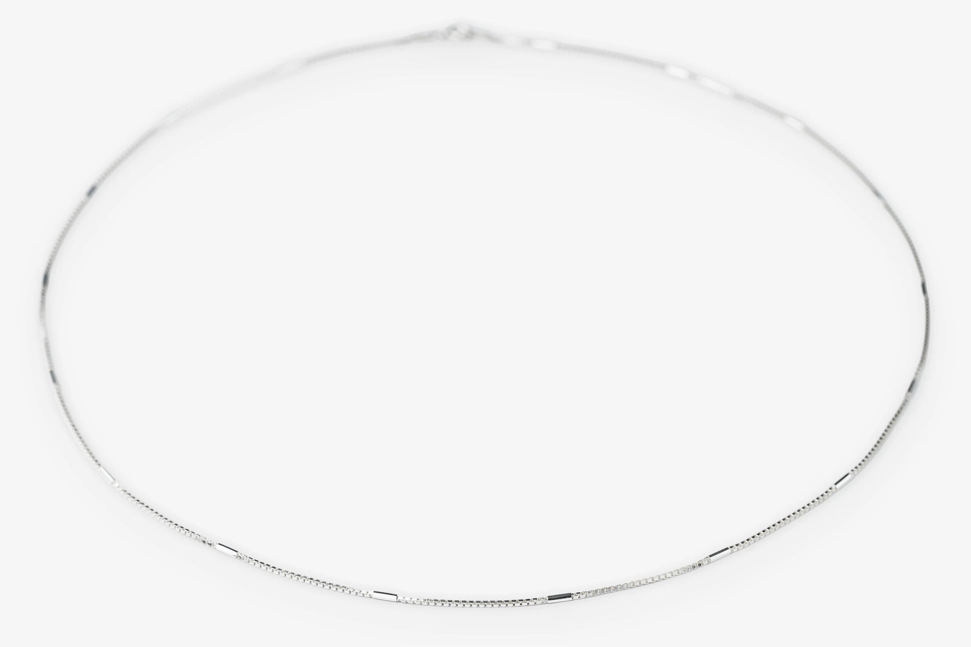 A delicate silver chain necklace arranged in a loose circle on a plain white background.