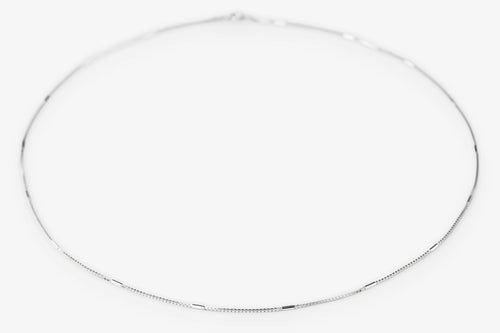 A delicate silver chain necklace arranged in a loose circle on a plain white background.