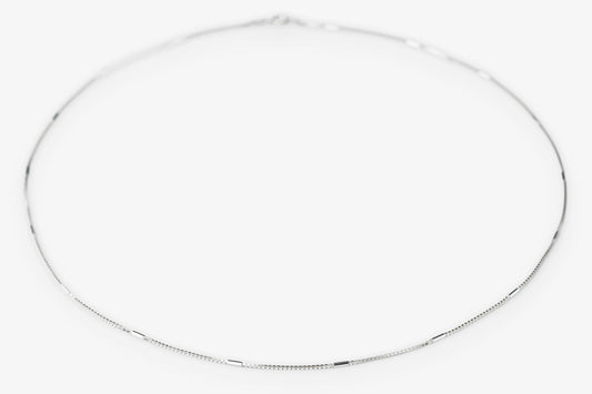 A delicate silver chain necklace arranged in a loose circle on a plain white background.