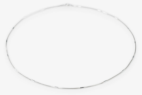 A delicate silver chain necklace arranged in a loose circle on a plain white background.