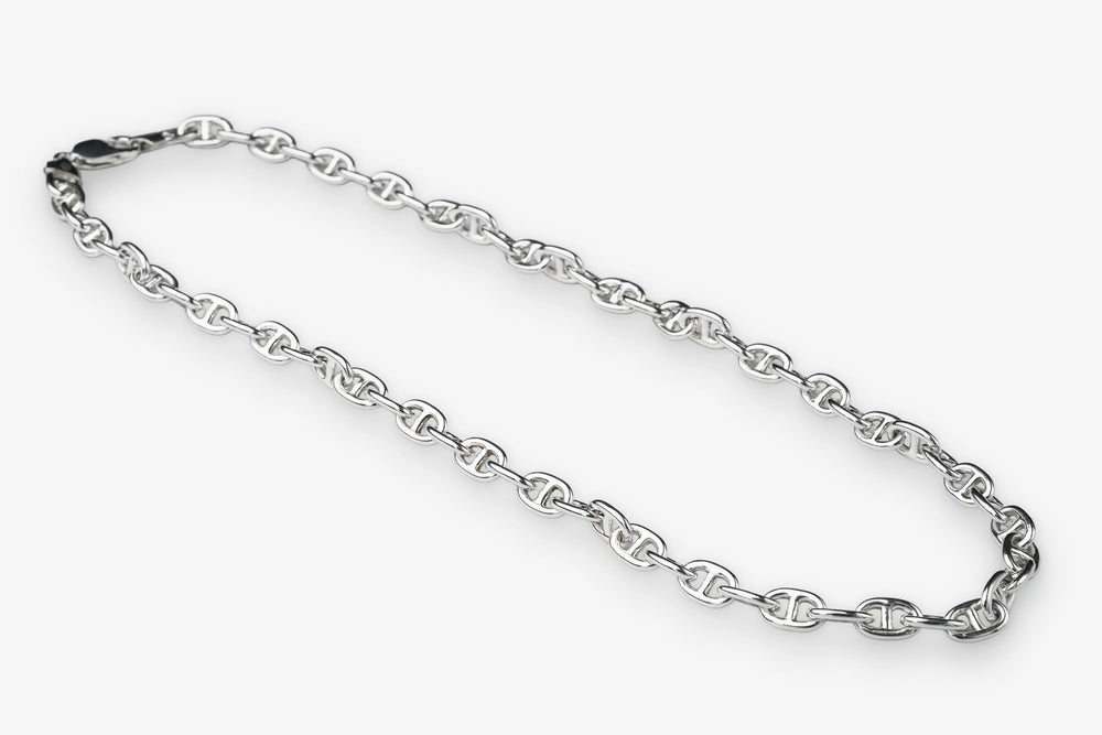 A silver-toned metal chain necklace with repeating interlocking links, arranged in a loose loop on a plain light gray background.